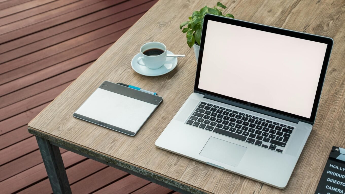 A minimalist outdoor workstation with laptop, coffee, and tablet on a rustic table.