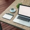 A minimalist outdoor workstation with laptop, coffee, and tablet on a rustic table.